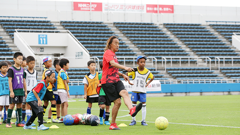 ニッパツ三ツ沢球技場でサッカー教室のコーチが子供向けに指導している様子